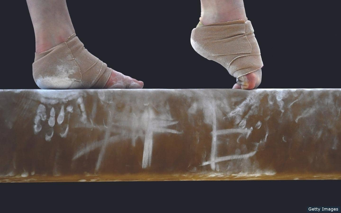 Close up shot of women's artistic gymnast feet on the balance beam. Feet are wrapped in athletic bandages and front toe is pointed in preparation to perform a skill.
