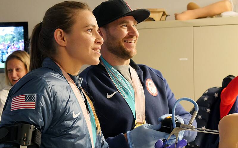 Paralympic gold medalist Mike Schultz tries his hand at arthroscopic knee surgery on a dummy limb while Oksana Masters, two-time Paralympic champion, looks on.