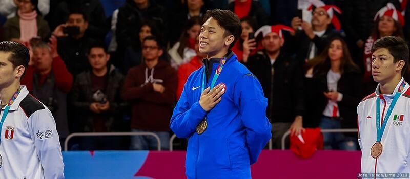Alex Lee stands on the podium and smiles as he listens to the US National Anthem, gold medal in men's poomsae hanging around his neck.