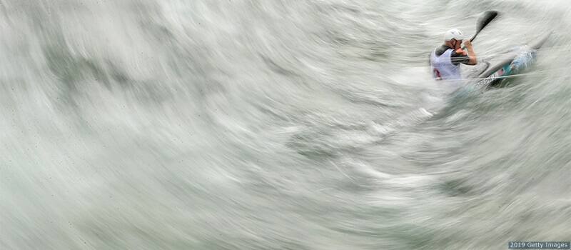 Team USA's Joshua Joseph competes in the men's kayak K1 semifinal. Photo is blurs the water into a half-pipe but captures Joseph crisply, mid-paddle, in the upper right. 