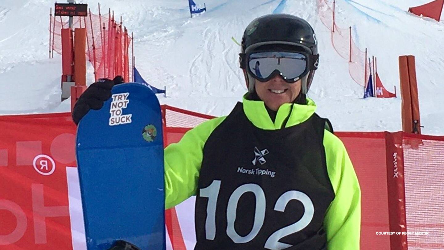 Peggy Martin poses with her snowboard in front of the slopes. 