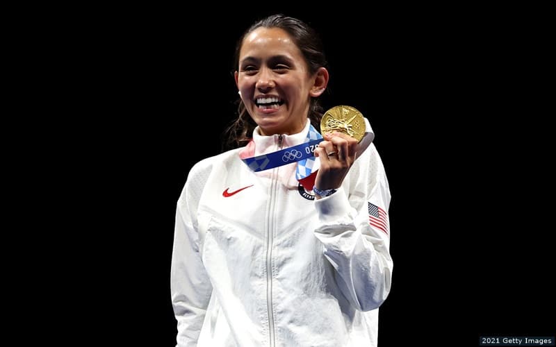 U.S. fencer Lee Kiefer smiles and holds a medal aloft after winning gold in the women's foil at the 2020 Olympic Games in Tokyo.