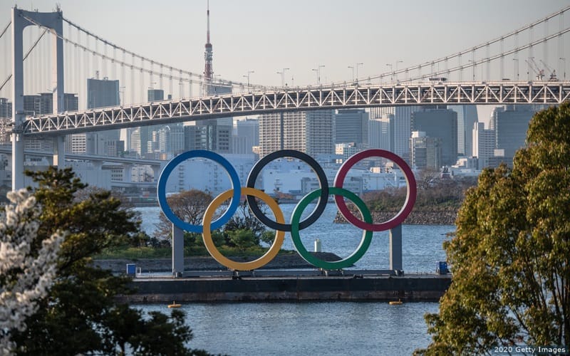 The Olympic rings sit in front of a river and bridge in Tokyo.