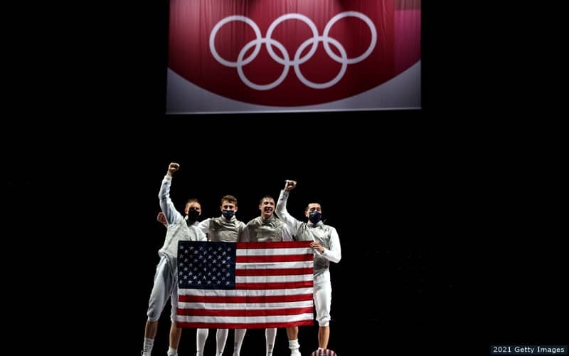 Four U.S. fencers hold the American flag and celebrate winning bronze in the men's team foil at the 2020 Olympic Games.