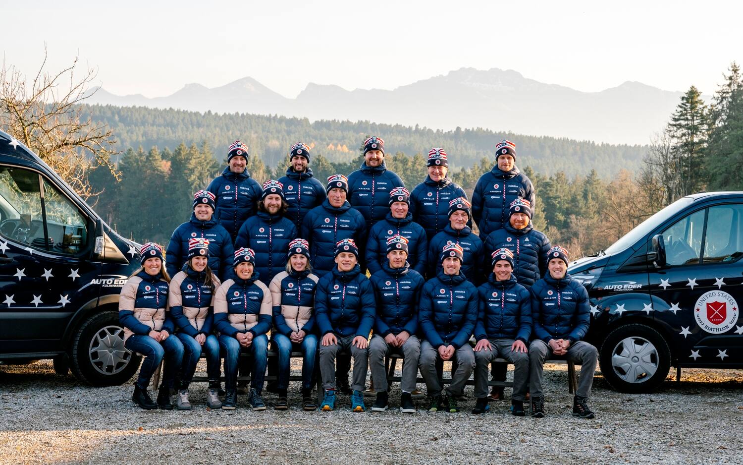 A team photo of the 2021-22 US Biathlon Team next to their official vehicles