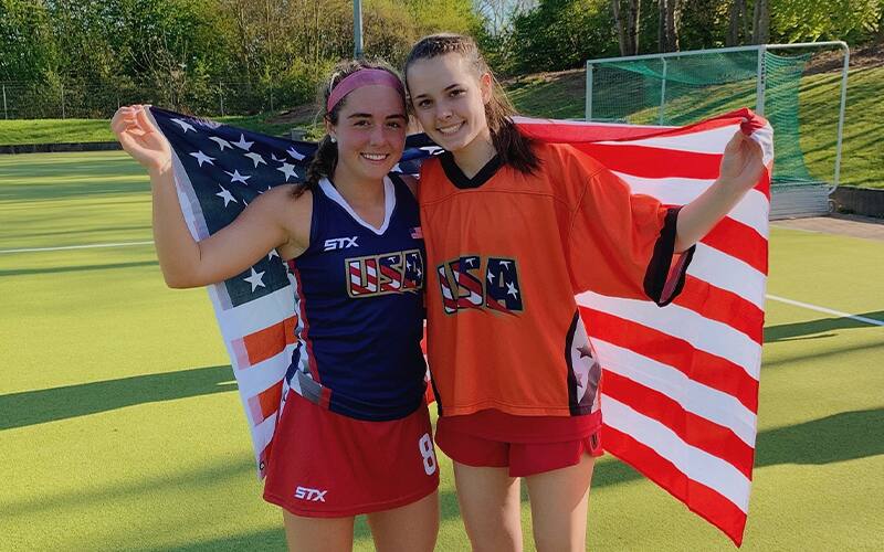Caylie McMahon and a teammate pose for a picture with the American flag dragged across their shoulders
