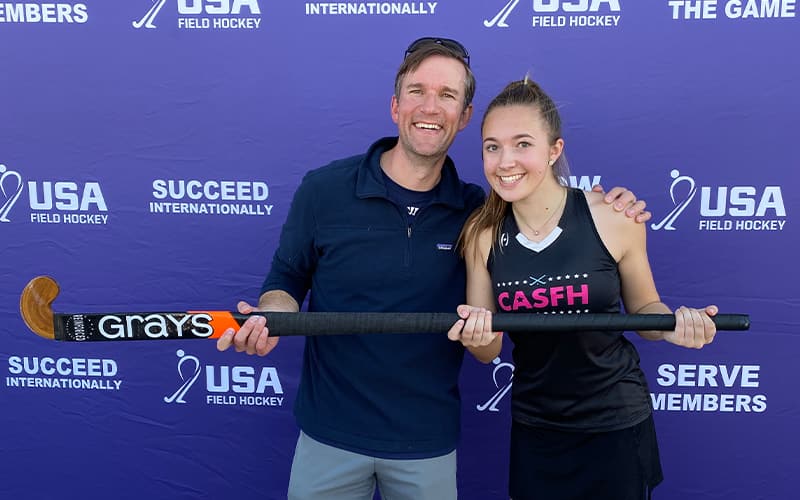 Elle Freeman and her dad pose at the National Hockey Festival with the large Gray's stick on stage