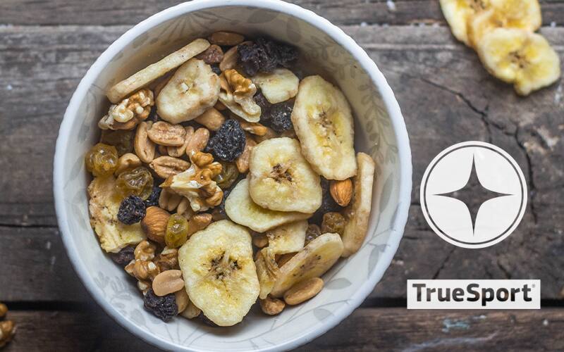 Bowl of cereal topped with bananas, raisins, walnuts and almonds with the TrueSport logo