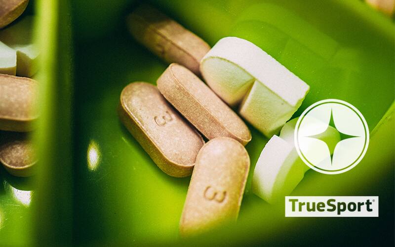 Supplement pills in a green container with TrueSport Logo