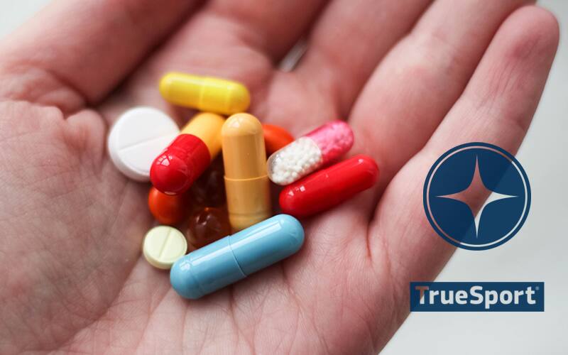 Hand holding supplement pills with TrueSport Logo