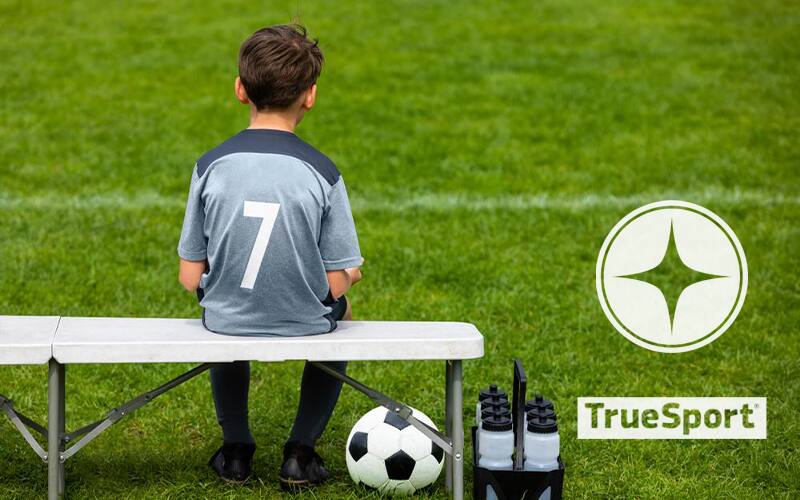Kid athlete sitting on a bench with the TrueSport logo