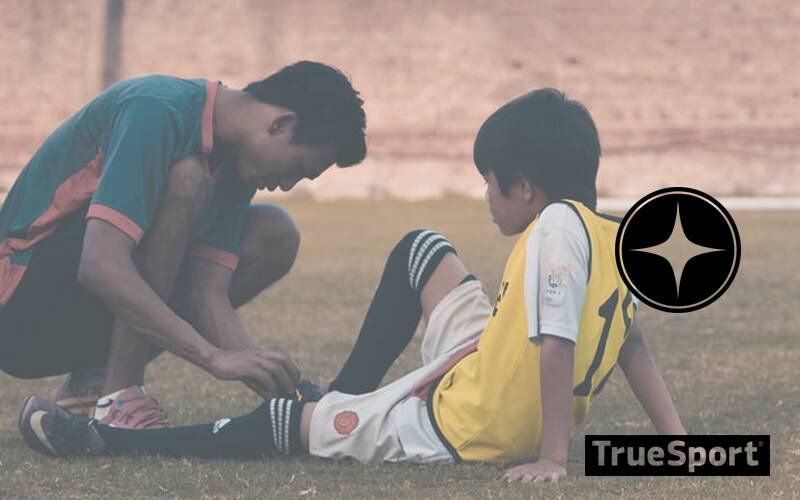 Coach helping athlete with leg injury on soccer field