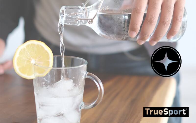 Water Pouring Out of Glass Jar into Glass with ice and a lemon slice on the side