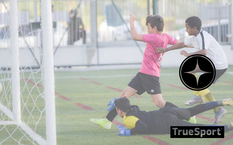 Athlete on soccer field, with boy in pink jersey going in to score