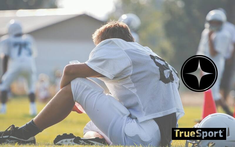 Football Athlete in white jersey sitting on football field
