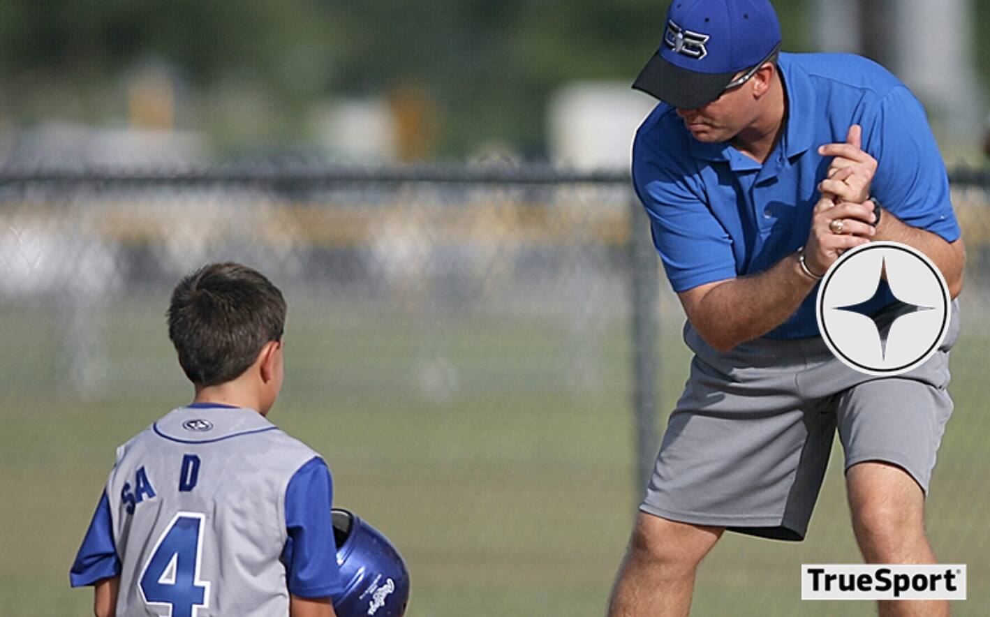 Coach teaching youth athlete to swing baseball bat