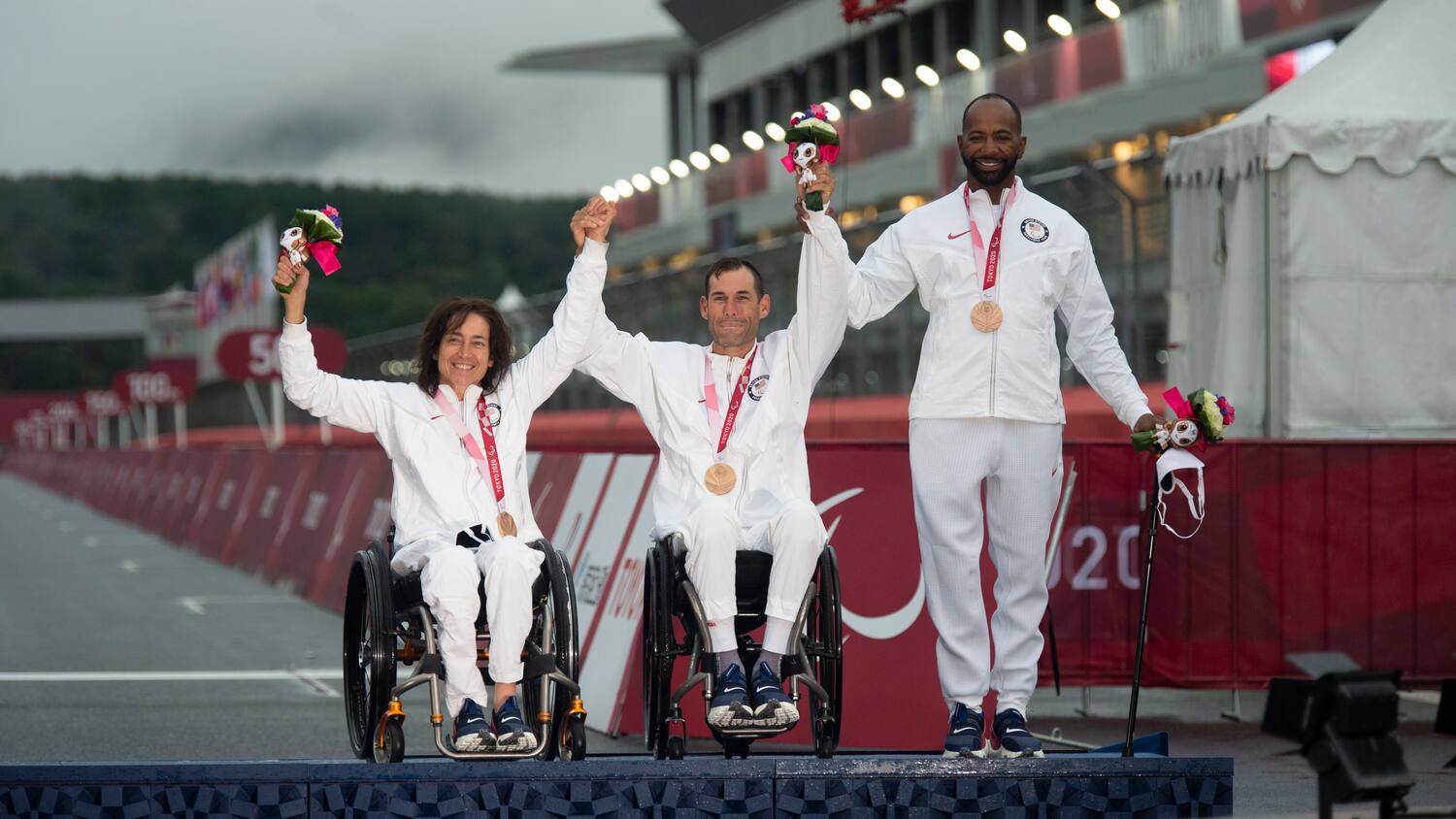 Alicia Dana, Ryan Pinney and Alfredo de los Santos pose on the podium with their bronze medals. All are smiling.