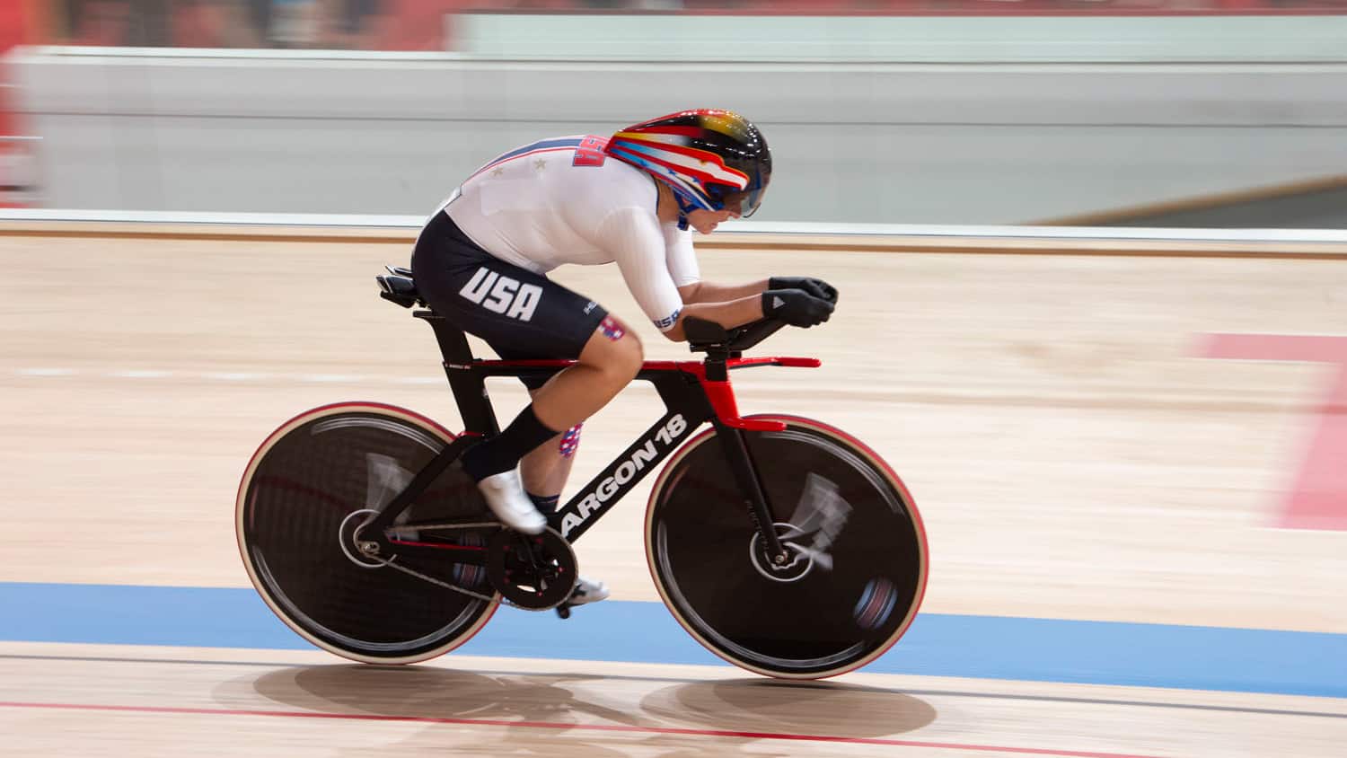 Shawn Morelli races on her bike on the track at Izu Velodrome while wearing her white Team USA uniform