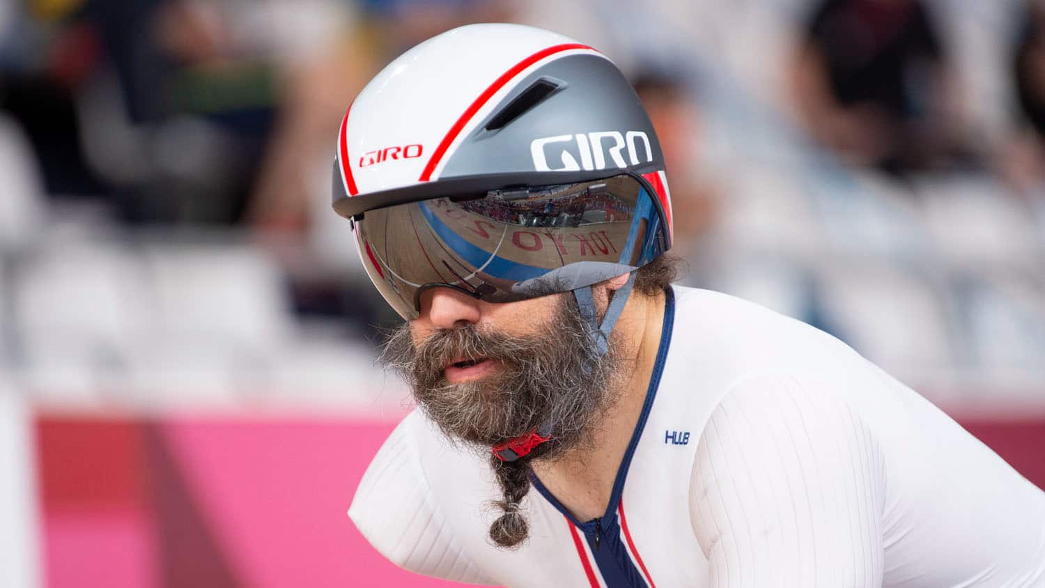 A chest up shot of Joe Berenyi wearing white uniform and black helmet with a reflection of the track in his goggle shades