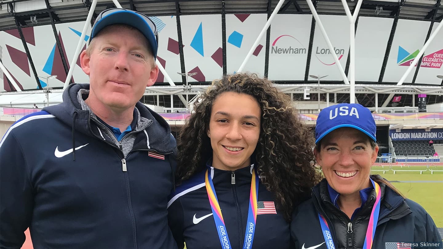 Two coaches and an athlete stand with medals in front of London stadium. 
