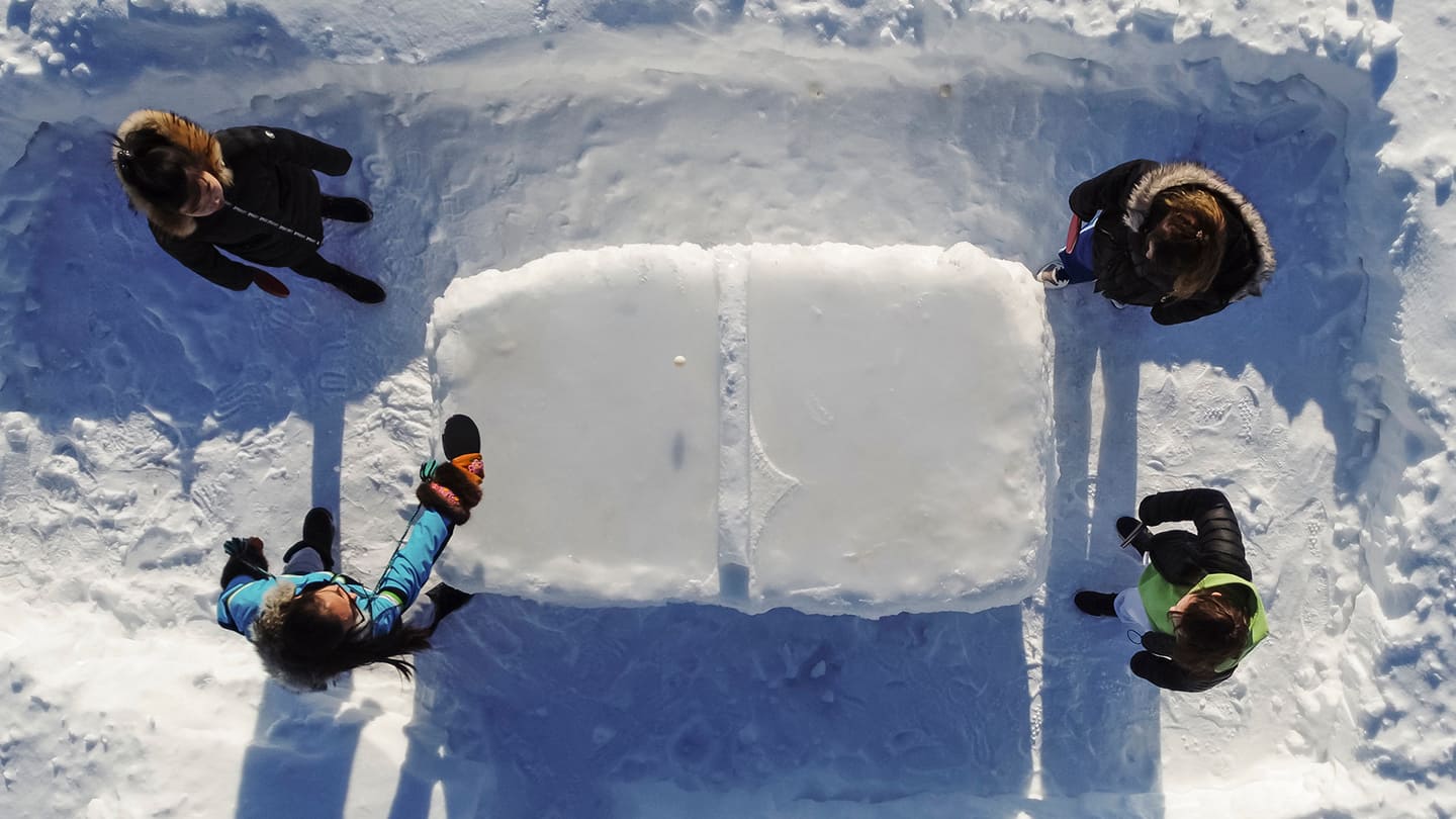 Sky view of 4 table tennis players playing table tennis out in the snow on a table made of ice.
