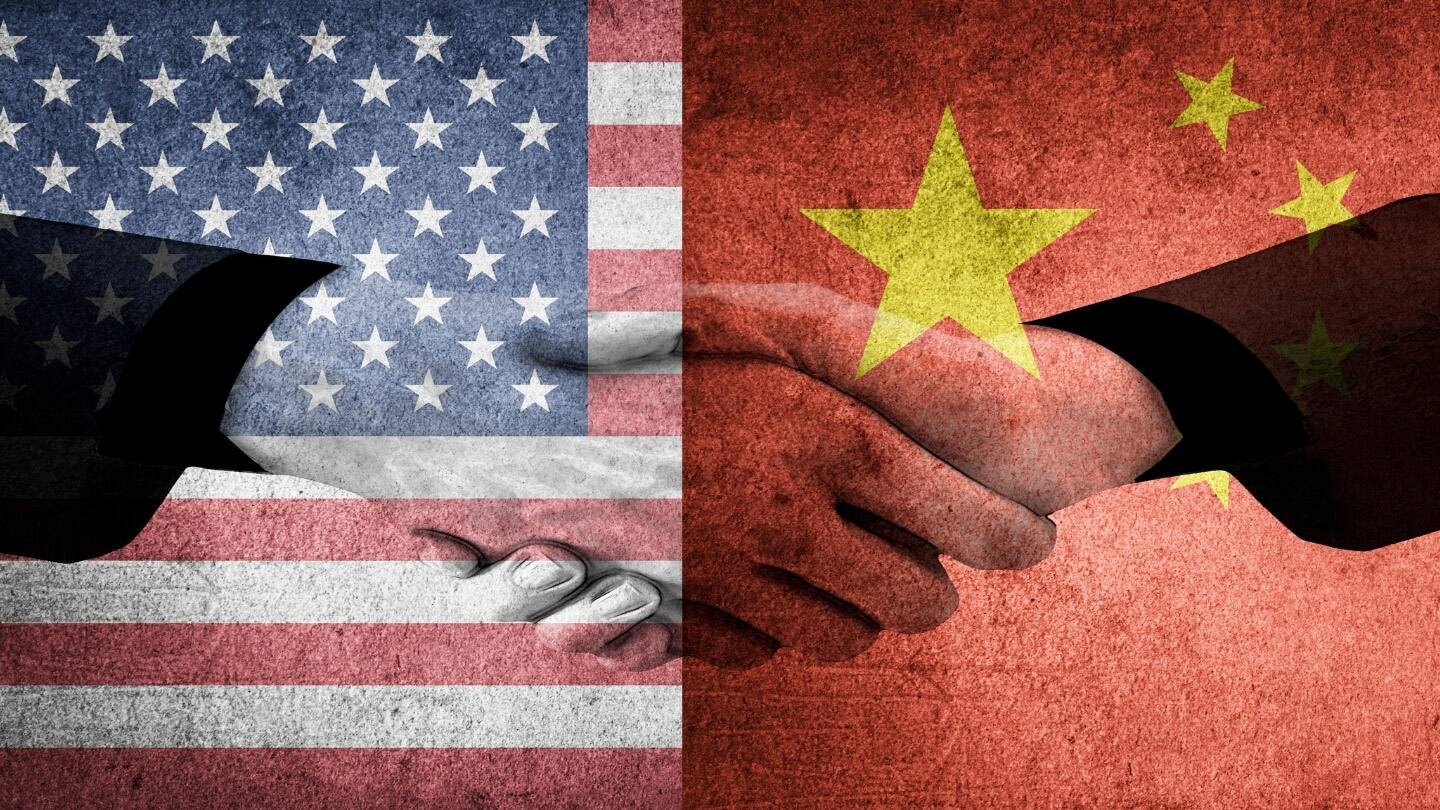 A pair of hands shaking over an American and Chinese flag in unity.