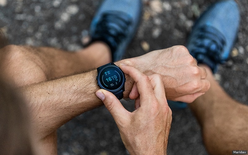 An athlete wearing running shoes adjusts his sport watch. 