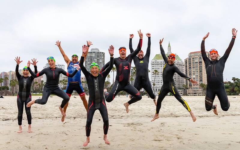 people in wetsuits jumping 