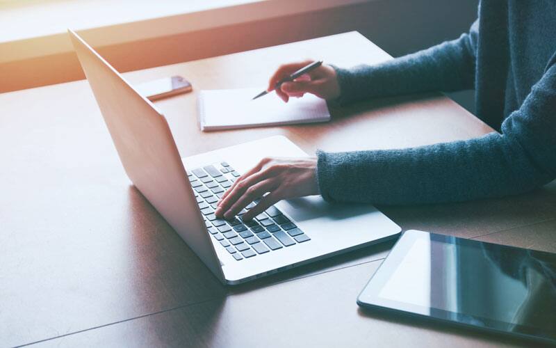 Using laptop and notepad to take notes