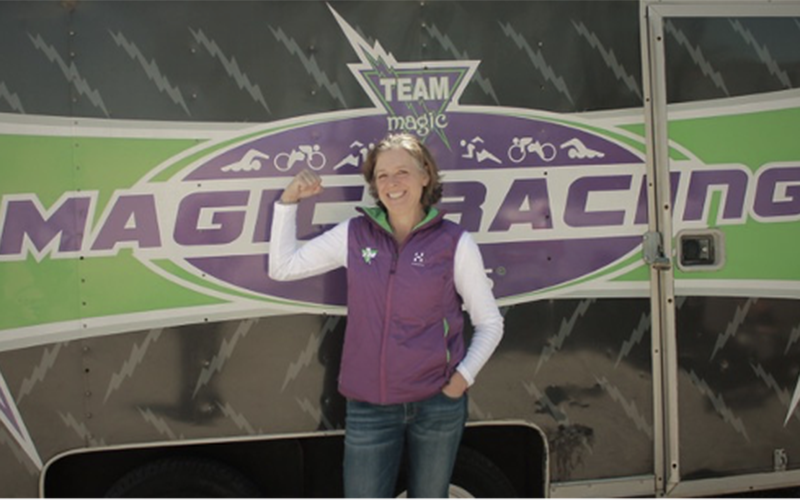 woman who is a race director wearing a purple vest and standing in front of a sign that reads Magic Racing