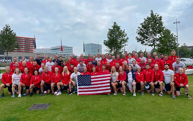 age group athletes from Team USA pose for a group photo will wearing red uniforms and standing together on green grass in Almere, The Netherlands