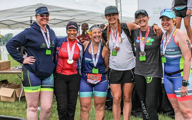 group of women posing together all wearing tri suits and medals around their necks