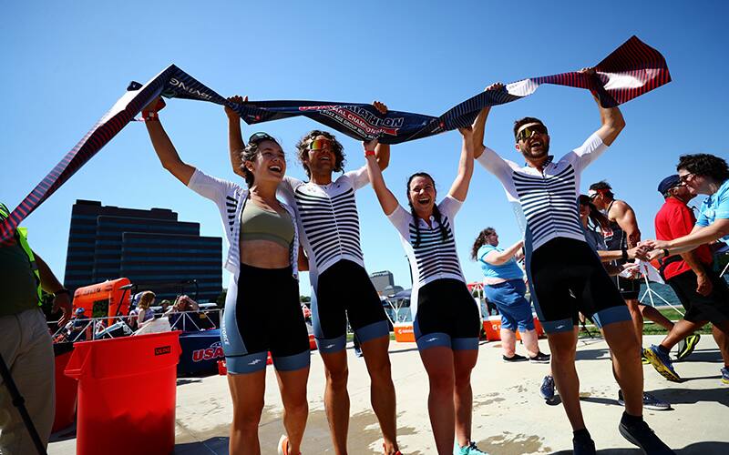 four athletes hold up the finish line tape after winning mixed relay national championships