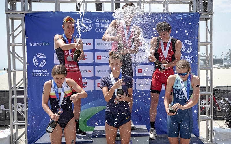 Athletes celebrate a champagne spray on the podium at the Americas Cup Long Beach
