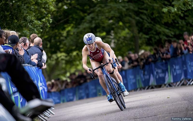 elite triathlete taylor spivey riding her bike. she is wearing a red USA jersey and a crowd of people are watchng