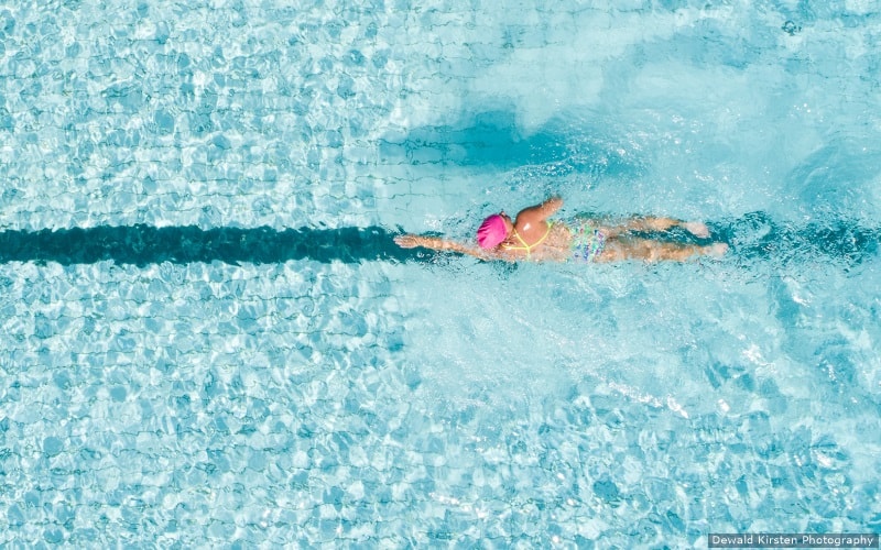 A swimmer swims in a pool. The water is clear and the swimmer is wearing a pink swim cap.