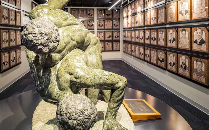The statue of ancient wrestlers with the Distinguished Member plaques in the background at the Wrestling Hall of Fame