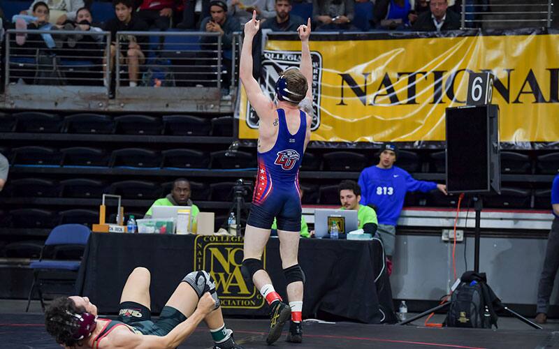 A Liberty University wrestler points to the sky after a big win at the 2022 NCWA Nationals