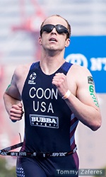 PTVI Paratriathlete Kyle Coon runs toward the finish line wearing a dark blue race tri suit with Coon written across his chest.